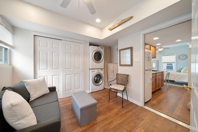 living area with ceiling fan, stacked washer and clothes dryer, and dark hardwood / wood-style flooring