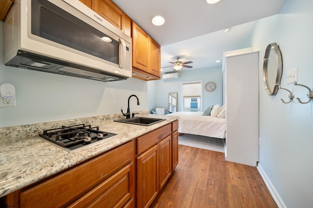 kitchen with dark hardwood / wood-style floors, stainless steel gas stovetop, sink, a wall mounted AC, and light stone countertops