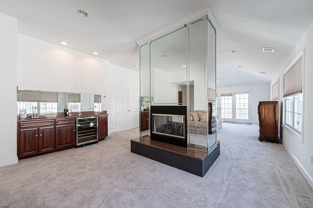 carpeted living room featuring wine cooler, a multi sided fireplace, lofted ceiling, and sink