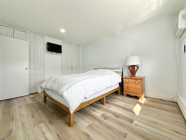 bedroom featuring a wall mounted air conditioner, light wood-type flooring, and two closets