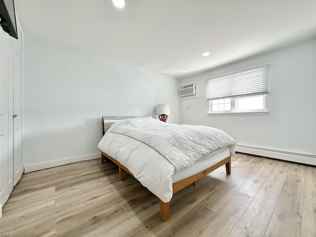 bedroom with a baseboard radiator, a wall unit AC, and light hardwood / wood-style floors