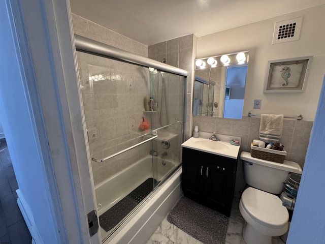 full bathroom with toilet, tile walls, vanity, enclosed tub / shower combo, and decorative backsplash