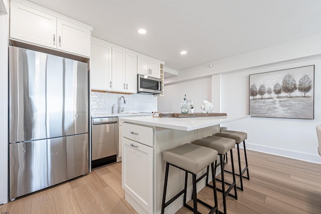 kitchen featuring stainless steel appliances, a center island, white cabinets, and light wood-type flooring