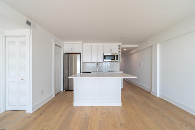 kitchen with a kitchen island, appliances with stainless steel finishes, white cabinetry, backsplash, and light hardwood / wood-style flooring