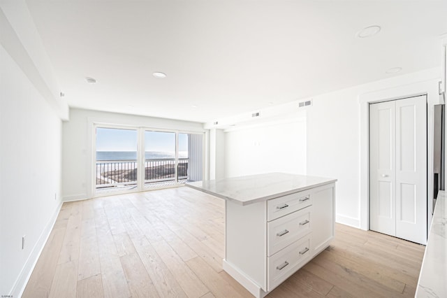 kitchen with a kitchen island, white cabinetry, a water view, light stone countertops, and light wood-type flooring