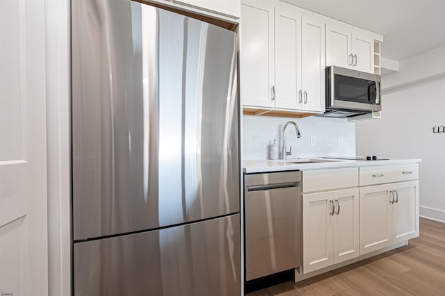 kitchen with white cabinetry, appliances with stainless steel finishes, light hardwood / wood-style floors, and backsplash