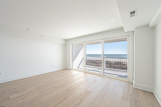 empty room featuring light hardwood / wood-style flooring, a beach view, and a water view