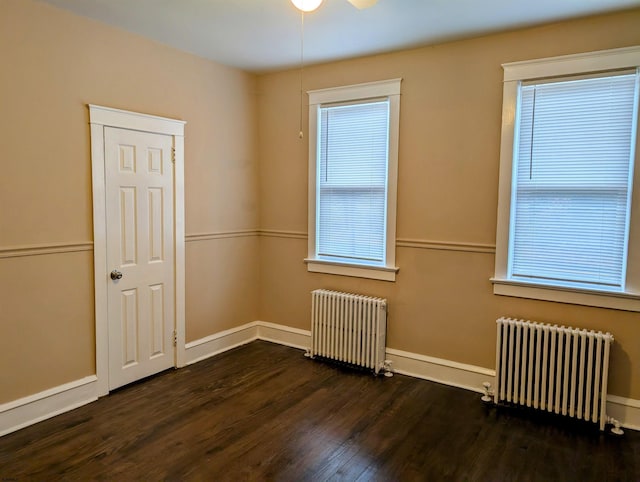 spare room with dark wood-type flooring, ceiling fan, and radiator