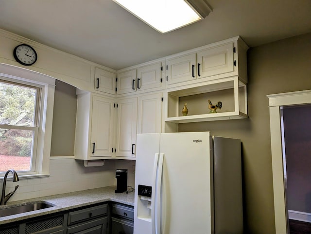 kitchen with tasteful backsplash, white cabinetry, sink, white fridge with ice dispenser, and light stone countertops