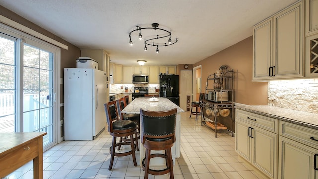 kitchen with light tile patterned floors, light stone counters, cream cabinets, and black appliances