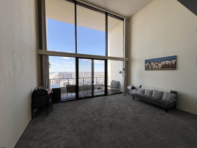 living room with a towering ceiling, expansive windows, and dark colored carpet