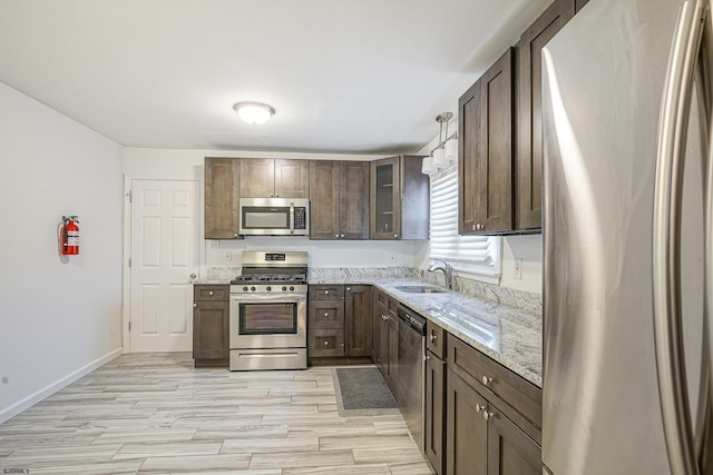 kitchen featuring appliances with stainless steel finishes, hanging light fixtures, light stone countertops, and dark brown cabinets