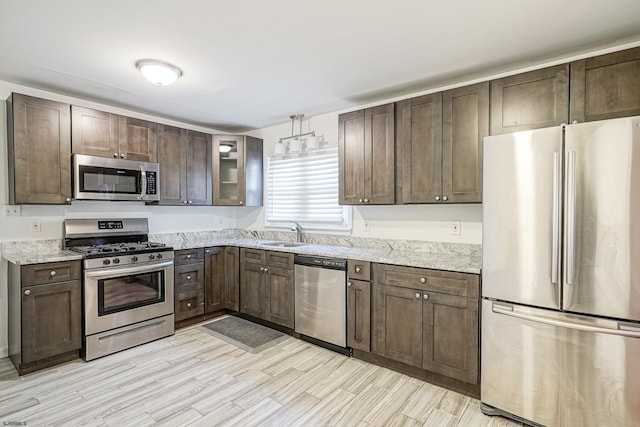 kitchen with appliances with stainless steel finishes, sink, dark brown cabinets, and light stone countertops