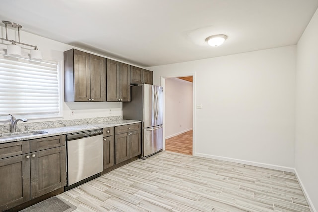 kitchen with stainless steel appliances, dark brown cabinetry, light hardwood / wood-style flooring, sink, and light stone counters