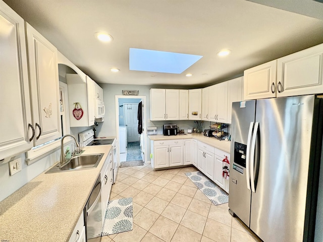 kitchen with stainless steel appliances, sink, light tile patterned floors, a skylight, and white cabinets