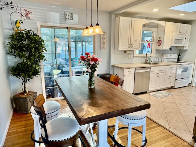 kitchen with white cabinetry, decorative light fixtures, light hardwood / wood-style floors, sink, and white appliances