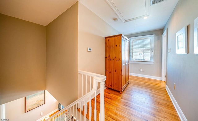 hallway with attic access, baseboards, light wood-style flooring, and an upstairs landing