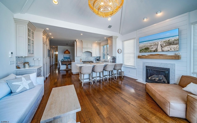 living room featuring an inviting chandelier, vaulted ceiling, and dark wood-type flooring