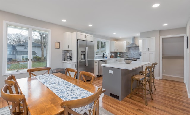 kitchen featuring stainless steel appliances, wall chimney range hood, a center island, sink, and white cabinetry