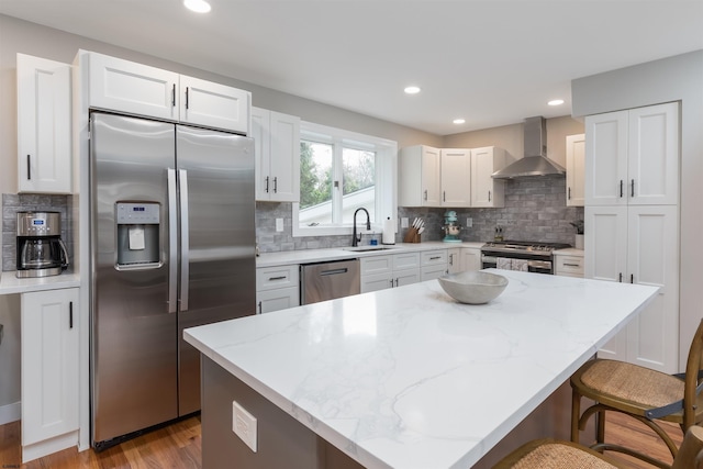 kitchen featuring appliances with stainless steel finishes, wall chimney exhaust hood, light stone counters, a center island, and white cabinetry