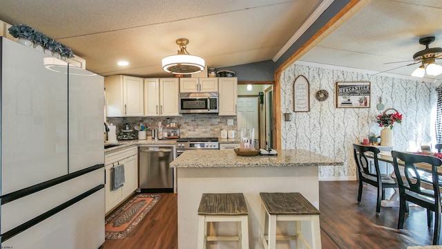 kitchen with appliances with stainless steel finishes, vaulted ceiling with beams, light stone counters, a breakfast bar, and a center island