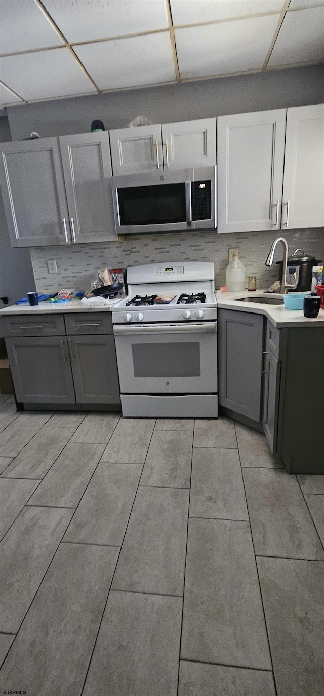 kitchen with a paneled ceiling, white range with gas cooktop, decorative backsplash, sink, and white cabinetry