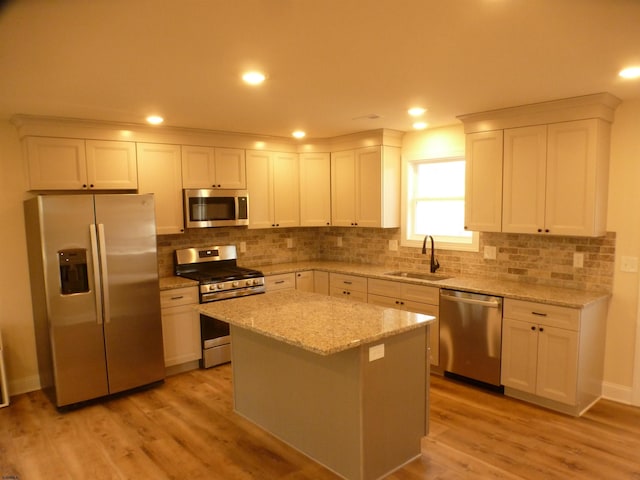 kitchen with sink, light stone counters, a center island, white cabinetry, and stainless steel appliances