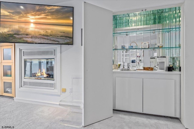 bar featuring a sink, a glass covered fireplace, and light colored carpet