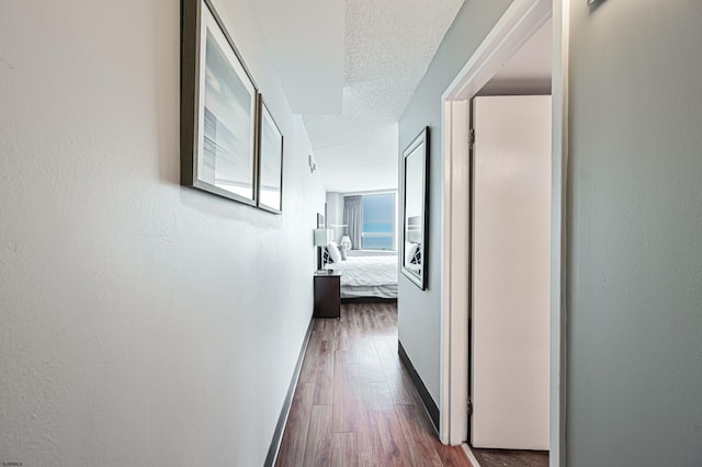 hall featuring a textured ceiling, wood finished floors, and baseboards