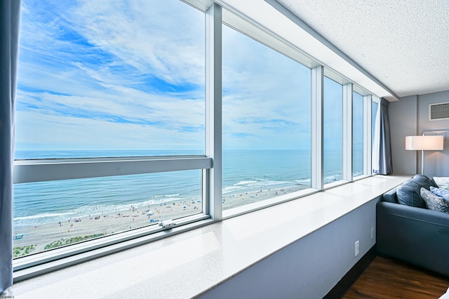 unfurnished living room featuring visible vents, dark wood-style flooring, a water view, a textured ceiling, and a view of the beach