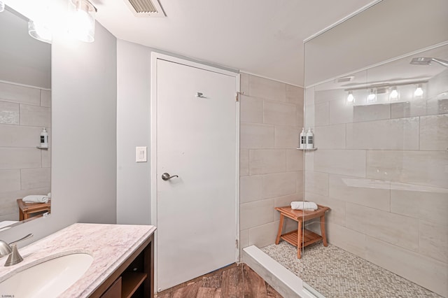 full bathroom featuring visible vents, tiled shower, wood finished floors, and vanity