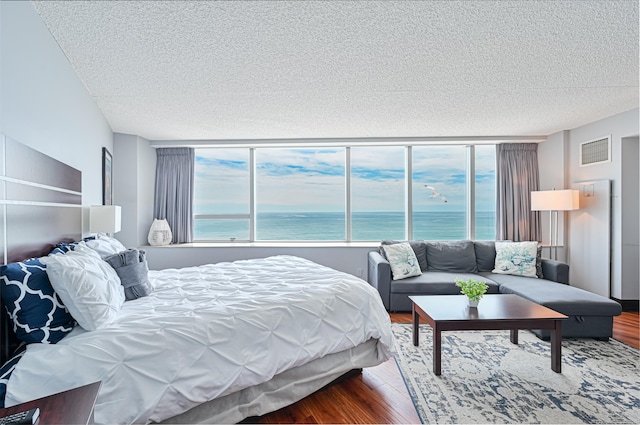 bedroom with a water view, multiple windows, visible vents, and wood finished floors