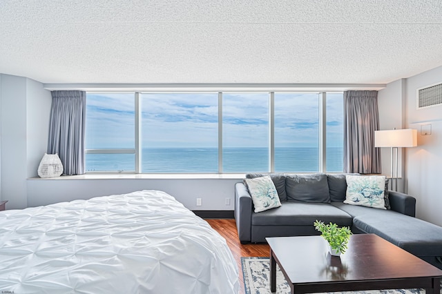 bedroom with a textured ceiling, a water view, wood finished floors, and visible vents