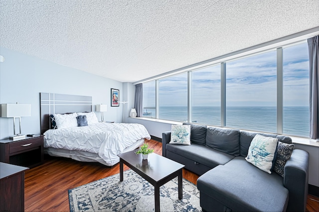 bedroom featuring a water view, a textured ceiling, and dark wood-type flooring