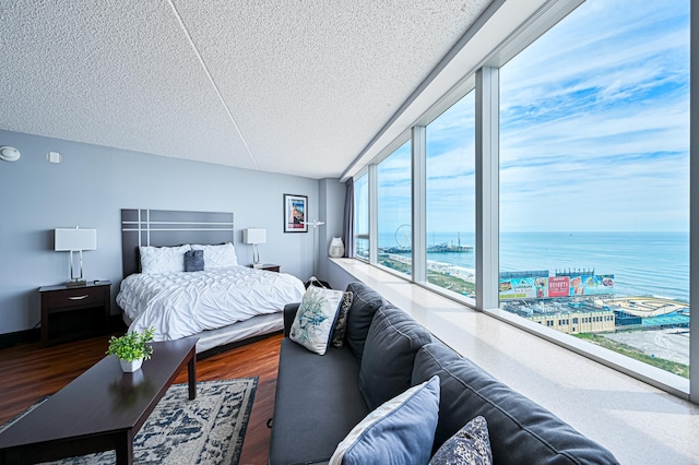 bedroom featuring a textured ceiling, a wall of windows, a water view, and dark wood-style floors