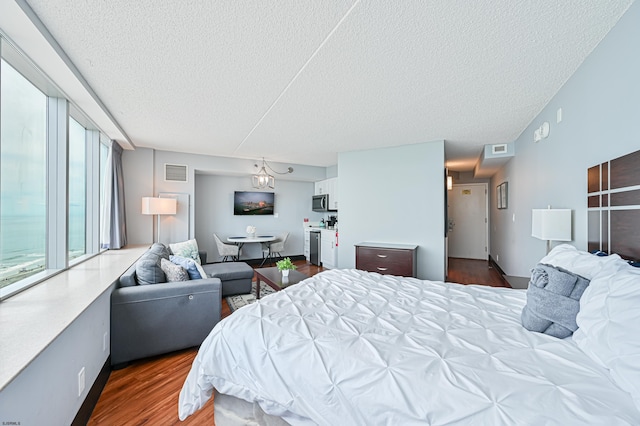 bedroom with a wall of windows, visible vents, a textured ceiling, and wood finished floors