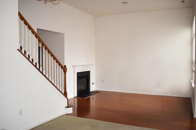 unfurnished living room featuring a fireplace with flush hearth, stairs, baseboards, and dark wood-type flooring