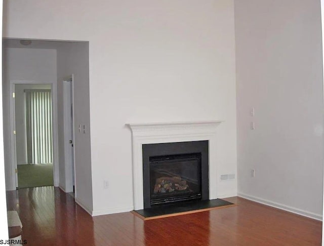 unfurnished living room featuring a fireplace with flush hearth, dark wood-style flooring, and baseboards