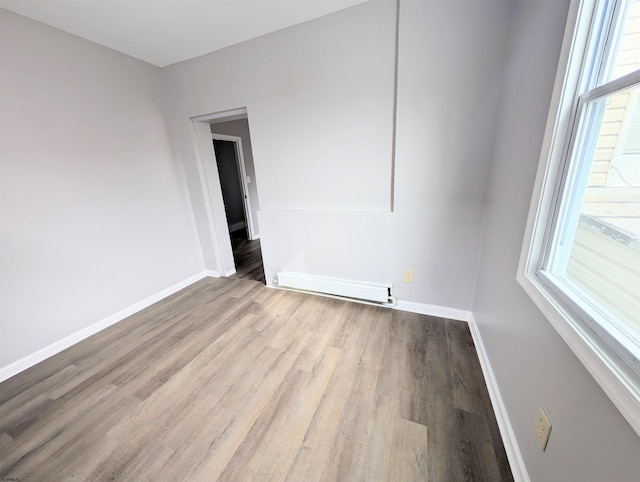 empty room with light wood-type flooring, a baseboard radiator, and baseboards