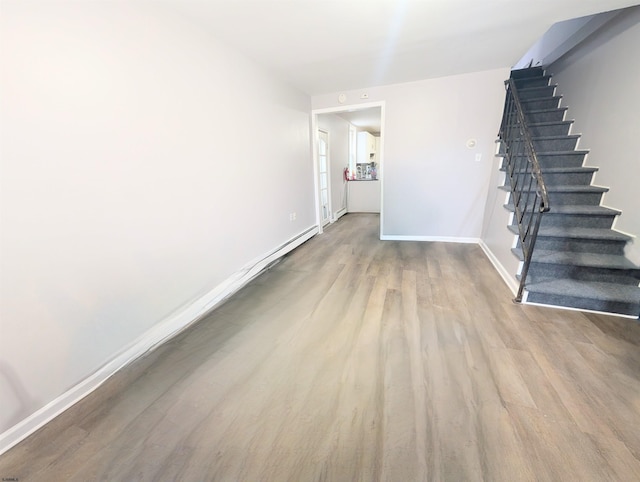 unfurnished room with stairway, light wood-type flooring, and baseboards