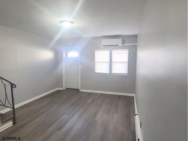 additional living space featuring dark wood-type flooring, a wall mounted air conditioner, and baseboards