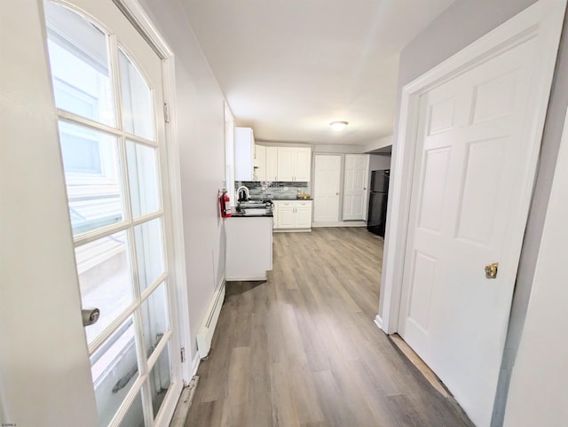 kitchen featuring dark countertops, decorative backsplash, baseboard heating, freestanding refrigerator, and white cabinets