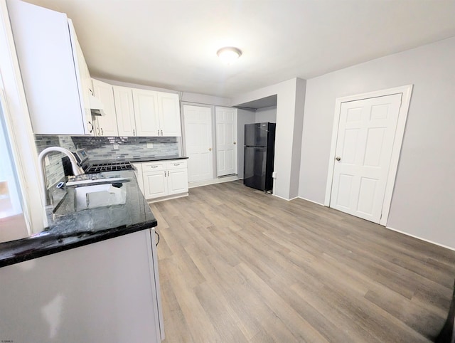 kitchen with a sink, light wood-style floors, white cabinets, backsplash, and freestanding refrigerator