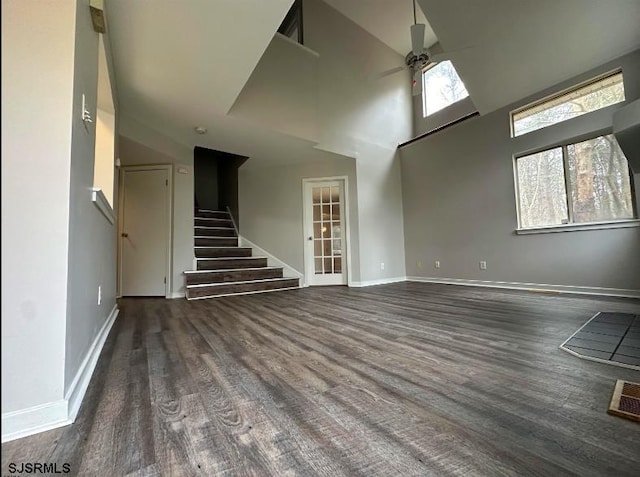 unfurnished living room with ceiling fan, dark wood-type flooring, a high ceiling, baseboards, and stairway