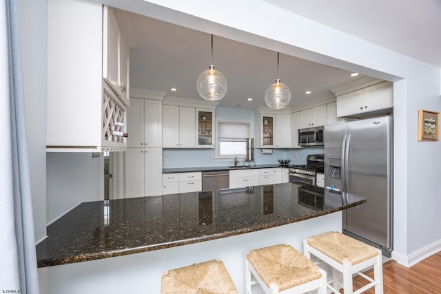 kitchen with decorative light fixtures, stainless steel appliances, glass insert cabinets, white cabinetry, and a kitchen bar