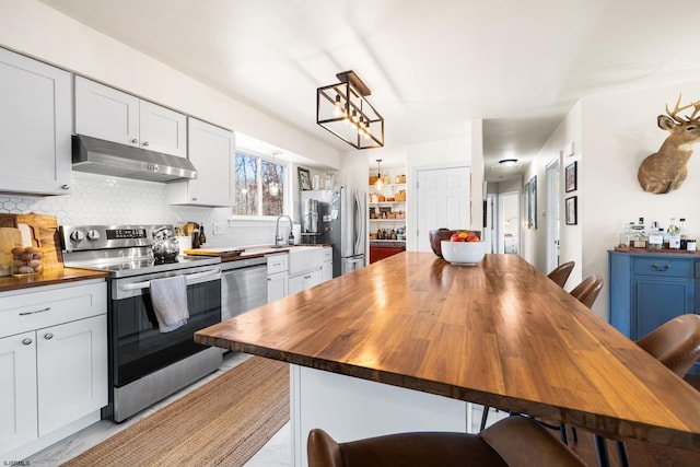 kitchen featuring stainless steel appliances, wooden counters, under cabinet range hood, and tasteful backsplash