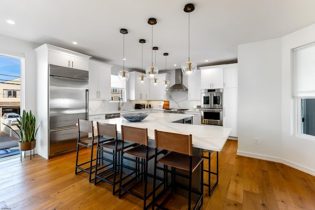 kitchen with white cabinets, a spacious island, wall chimney exhaust hood, stainless steel appliances, and pendant lighting