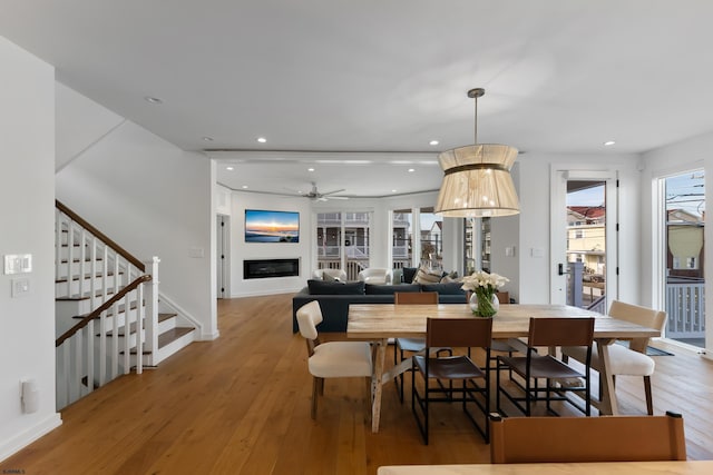 dining area featuring recessed lighting, a ceiling fan, a glass covered fireplace, wood finished floors, and stairs