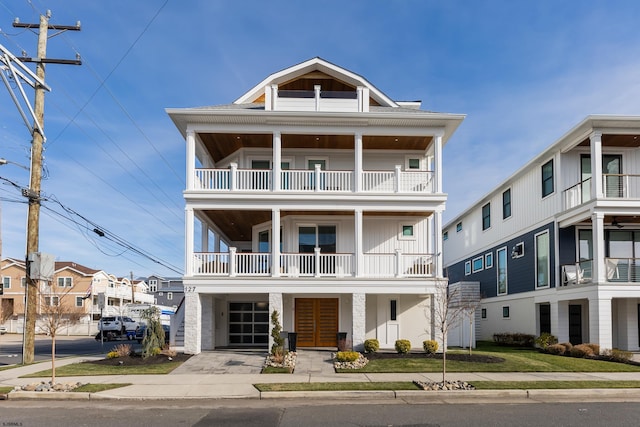 coastal inspired home with board and batten siding, a balcony, a residential view, and concrete driveway