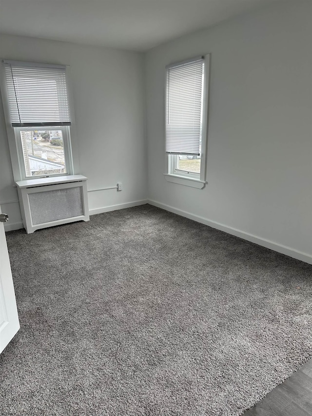 spare room featuring radiator heating unit, dark carpet, and baseboards